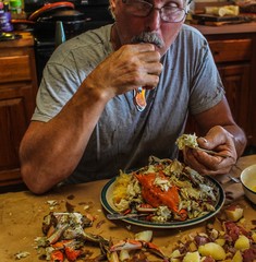 Older man with very strong looking hands eating a crab at a traditional Cajun seafood boil served steaming hot on brown paper