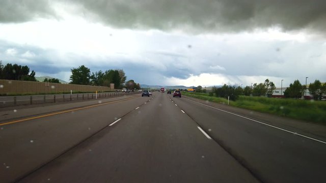 A car is driving through a storm. Water is lightly dropping on the windshield. Cars are seen driving by on the freeway.