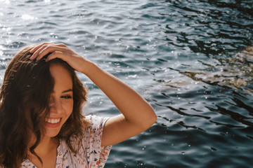 Young latin woman smiling with the blue sea in the background. The waves behind her reflecting the...