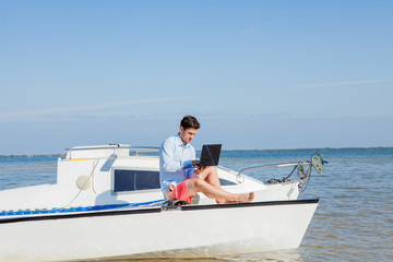 Young and handsome man with laptop computer on sailboat. Freelance work concept