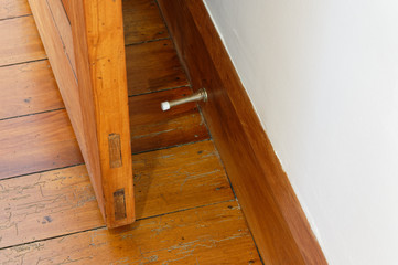 A wooden door is prevented from hitting a white wall by the metal spring door stopper that is attached to the wooden skirting board