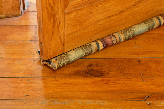 A material draught stopper under a wooden door, wood worm marks can be seen in the wooden floor