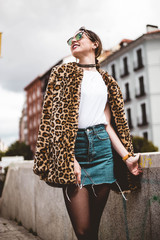 Stylish portrait of young woman looking aside smiling and wearing trendy animal, leopard print faux...