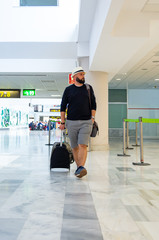 Young man walking through an airport terminal carrying a suitcase