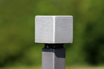 Light grey metal cube mounted on top of wrought iron fence in local garden on warm sunny summer day