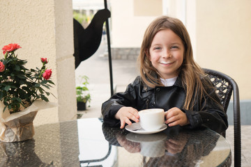 Little prankster schoolchild enjoys a coffee drink. She is pleased and happy. Milk foam on his face...