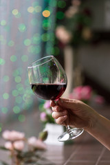 Hand sommelier holding glass of red wine. Glass of red wine on background of colorful bar. Bokeh. Cold toning. Space for text. Concept alcoholic drinks. 