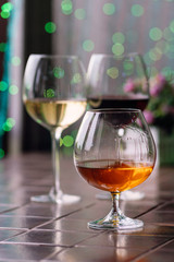Brandy in typical snifter. Cognac in elegant glass with space for text on colorful background. Two glasses of wine in background unfocus. Tasting, restaurant. Concept alcoholic drinks.