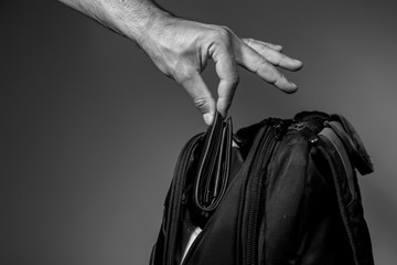Black and white photo of a thief's hand pulling a purse from a backpack on a gray background
