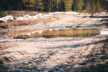 Deep spring puddle on the sandy road due to melting snow after winter.