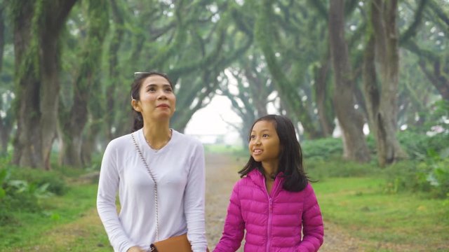 Happy little girl and her mother walking at the park with green trees in De Djawatan forest, East Java, Indonesia. Shot in 4k resolution