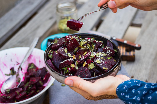 Sweet beetroot salad. Cooked with olive oil, vinegar, pumpkin and sesame seeds , herbs in bowl. Woman hands holds beet salad.
