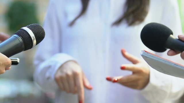Journalists holding microphones interviewing famous woman gesturing hands, news