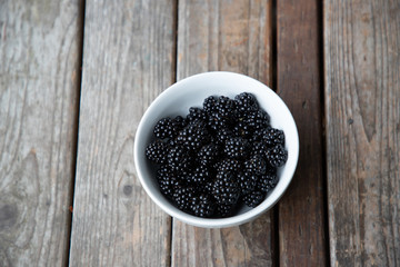 fresh blackberries in a white bowl on a wood background