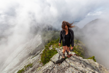 Naklejka premium Adventurous Girl is hiking up a steep trail up a beautiful rocky mountain during a cloudy summer morning. Taken on Crown Mountain, North Vancouver, BC, Canada.