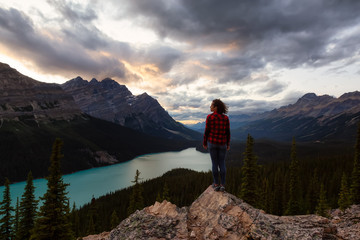 Adventurous girl standing on the edge of a cliff overlooking the beautiful Canadian Rockies and Peyto Lake during a vibrant summer sunset. Taken in Banff National Park, Alberta, Canada.