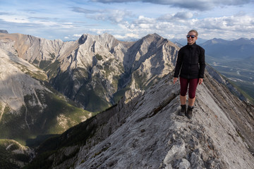 Obraz premium Adventurous Girl is hiking up a rocky mountain during a cloudy and rainy day. Taken from Mt Lady MacDonald, Canmore, Alberta, Canada.