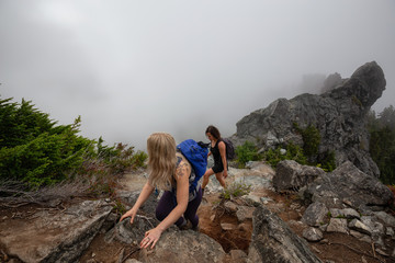 Obraz premium Adventurous Girl is hiking up a steep trail up a beautiful rocky mountain during a cloudy summer morning. Taken on Crown Mountain, North Vancouver, BC, Canada.