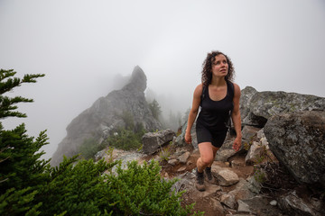 Obraz premium Adventurous Girl is hiking up a steep trail up a beautiful rocky mountain during a cloudy summer morning. Taken on Crown Mountain, North Vancouver, BC, Canada.
