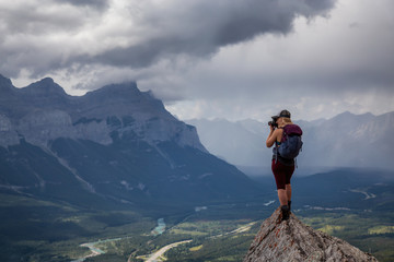 Adventurous Girl taking pictures on top of a rocky mountain during a cloudy and rainy day. Taken...