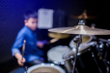 Selective focus to cymbals of drum set with blurry kid learning and play drum set with teacher in...