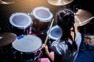 Fototapeta na wymiar Asian girl learning and play drum set with wooden drumsticks in music room. The concept of musical instrument, Top view to drum player and selective focus.