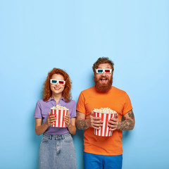 Studio shot of amused happy red haired boyfriend and girlfriend entertained in cinema, wear 3d...