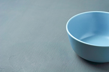 Deep empty ceramic bowl of blue color lies on dark concrete background. Space for text