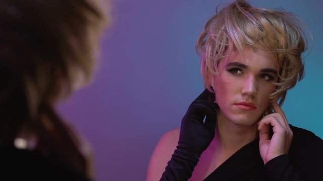 Man with makeup trying on blond female wig, male gender discomfort, transsexual