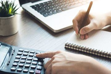 Business accountant man is using the calculator to calculate the income while taking the note on...