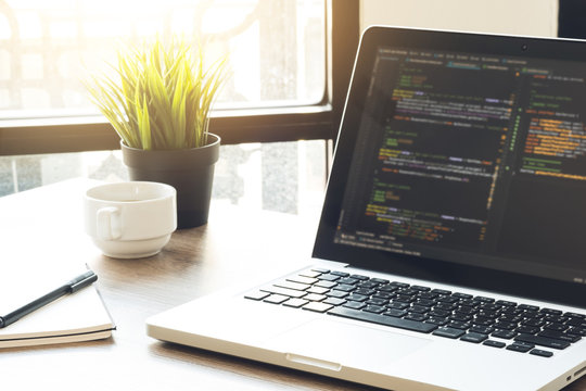 Wood software developer or programmer office desk table with laptop with the software code on the screen.