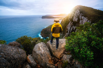 Young man trekker hiking on beautiful coast cliff of Tasman National Park in Tasman peninsula, Three Capes Track near Port Arthur in Tasmania, Australia. - obrazy, fototapety, plakaty