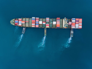 Widok z góry z lotu ptaka Holownik pchający kontenerowiec na nabrzeże w celu załadunku / rozładunku kontenera za pomocą dźwigu dla logistyki, eksportu importu, wysyłki lub transportu. - 285880645
