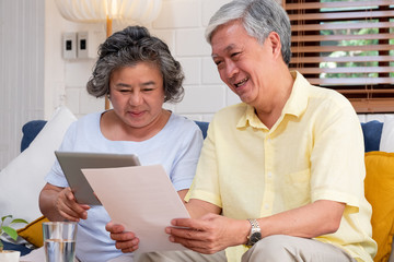 Asian senior couple use tablet searching about retirement financial document sitting on sofa at home,senior learn to use technology.aging in place concept