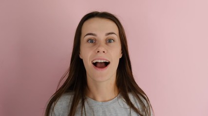 Close up portrait of surprised woman  with flying hair and mouth wide open. Portrait of good-looking carefree female, has long hair, isolated over pink background. People emotion