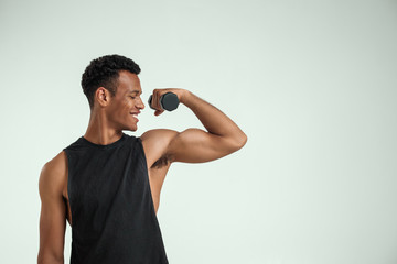 Making perfect body. Muscular young african man exercising with dumbbells and smiling while...
