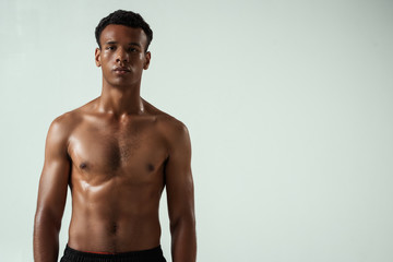 Fototapeta premium After workout. Portrait of young shirtless muscular african man looking at camera while standing against grey background
