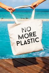 Kids hand holding eco bag with sign NO MORE PLASTIC on blue sea tropical background, safe environment concept