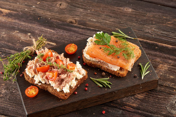 Sandwiches with salmon and tuna and butter on bread on a cutting board on a wooden table