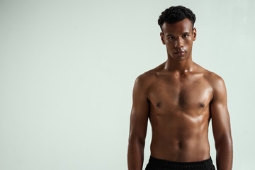 Strong and confident. Portrait of young shirtless muscular african man looking at camera while standing against grey background
