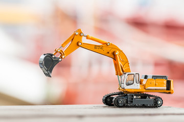 Yellow excavator model toy parked on floor ground on a construction site background.