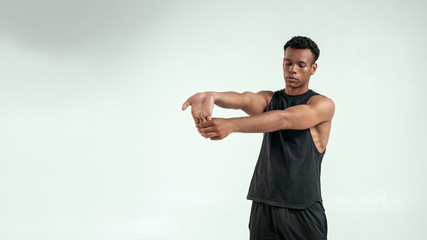 Naklejka premium Before training. Strong young afro american man warming up while standing against grey background