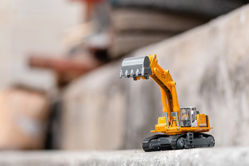 Yellow excavator model toy performs excavation work on a construction site. (Image stacking...