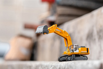 Yellow excavator model toy performs excavation work on a construction site. (Image stacking technique)