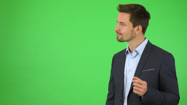 A young handsome businessman smiles at the camera, there are objects in front of him and he sends them with his finger up and to the side - green screen studio