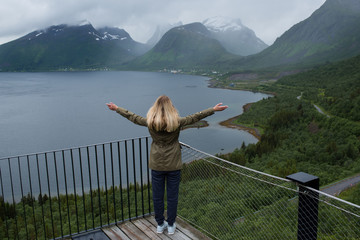 Girl on the observation deck enjoys scenic view on the fjord. Top viewing platform. Ocean and mountain landscape. Wanderlust. Adventure, freedom, lifestyle. Explore North Norway. Summer in Scandinavia