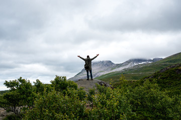 A man stands on top and enjoys a stunning view. Mountain beautiful landscape. Dramatic sky. Enjoy the moment, relax. Wanderlust. Adventure, freedom, lifestyle. Explore North Norway. Summer Scandinavia