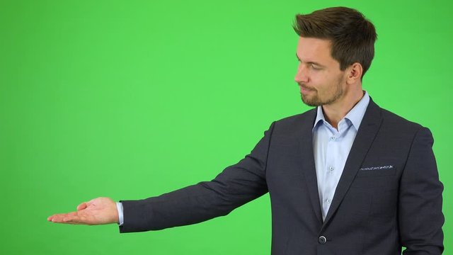 A young handsome businessman puts out a hand with a product, occasionally moving it to the side while he smiles and nods - green screen studio