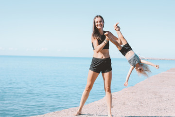 Young fit woman mom with little cute girl exercising on beach together, healthy lifestyle, dynamic gymnastic