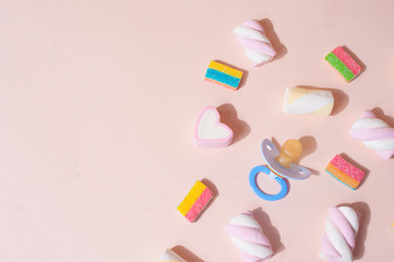 Pastel light pink background wih light blue pacifier and colorful candies flat lay top view
